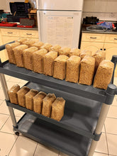 Load image into Gallery viewer, A three-tier gray utility cart loaded with multiple clear plastic bags filled with a tan-brown granular substance, photographed in a lab environment.