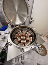 Load image into Gallery viewer, A stainless steel pressure cooker or sterilizer with its lid open, showing several brown rectangular blocks wrapped in white material inside a steaming basket, set on a tiled countertop in a kitchen-like environment.