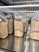 Load image into Gallery viewer, Several clear plastic bags filled with a beige and brown granular material, likely bedding or substrate, arranged on a stainless steel shelf.