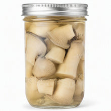 Load image into Gallery viewer, A clear glass mason jar with a silver metal lid, filled with sliced and whole mushrooms submerged in amber-colored liquid, shown on a white background.
