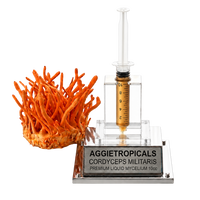 A 10cc liquid mycelium starter kit by Aggietropicals, featuring an orange Cordyceps militaris fruiting body next to a clear plastic syringe filled with amber-colored liquid on a clear acrylic stand with a silver metal base.