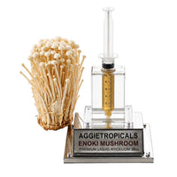 A cluster of Enoki mushrooms with long thin stems and small tan caps, beside a syringe filled with liquid mycelium culture mounted on a mirrored stand, labeled "AGGIETROPICALS, ENOKI, PREMIUM LIQUID MYCELIUM 10cc", on a white background.