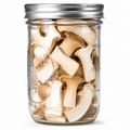 A clear glass mason jar with a silver metal lid, filled with sliced dried mushrooms, shown against a plain white background.
