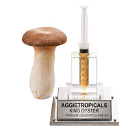 A cluster of King Oyster mushrooms with thick white stems and small dark brown caps, beside a syringe filled with liquid mycelium culture mounted on a mirrored stand, labeled "AGGIETROPICALS, KING OYSTER, PREMIUM LIQUID MYCELIUM 10cc", on a white background.