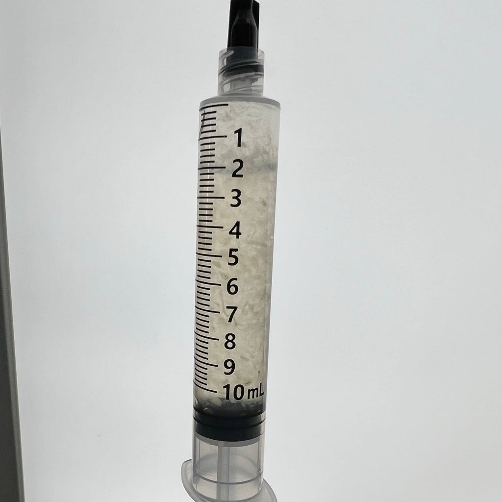 A 10 mL medical-style syringe with black measurement markings and a black plunger top, held upright by a gloved hand against a plain light background.