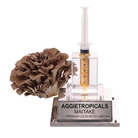 A Maitake mushroom formed of overlapping grey-brown fan-shaped caps in a dense rosette, beside a syringe filled with liquid mycelium culture mounted on a mirrored stand, labeled "AGGIETROPICALS, MAITAKE, PREMIUM LIQUID MYCELIUM 10cc", on a white background.