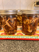 Load image into Gallery viewer, Several glass mason jars filled with sliced brown mushrooms in liquid, arranged on a patterned cloth over a speckled countertop in a kitchen setting.
