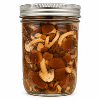 A clear glass mason jar with a silver metal lid, filled with pioppino mushrooms submerged in a liquid, photographed on a plain white background.