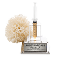 A 10ml syringe filled with golden liquid mycelium displayed in a clear acrylic holder on a silver metal base engraved with 'AGGIETROPICALS TREMELLA PREMIUM LIQUID MYCELUM 10cc'. A natural white sponge is positioned to the left of the syringe on a clean white background.