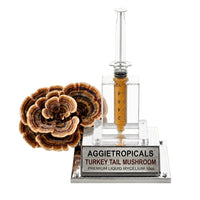 A Turkey Tail mushroom formed of thin fan-shaped caps with multicolored bands, beside a syringe filled with liquid mycelium culture mounted on a mirrored stand, labeled "AGGIETROPICALS, TURKEY TAIL, PREMIUM LIQUID MYCELIUM 10cc", on a white background.